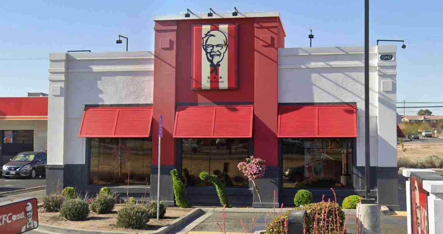 KFC restaurant with red facade and a large Colonel Sanders sign above the entrance on a sunny day.